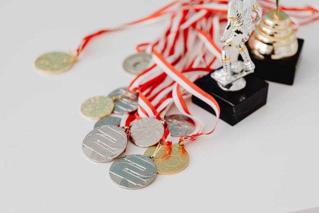 A varied collection of silver and gold medals alongside trophies on a white surface, showcasing achievement.